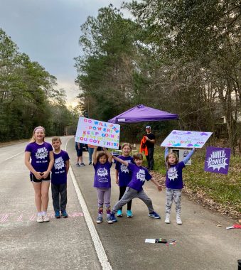 help | Sanfilippo Syndrome News | photograph of several purple-clad children standing on the side of a highway, with a purple tent behind them