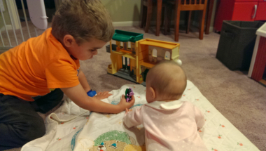 sister | Sanfilippo Syndrome News | photo of a young boy in an orange shirt, at left, reaching out to a toddler to his right
