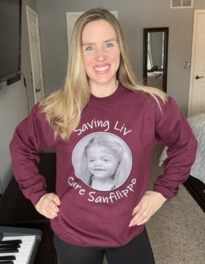 A woman stands indoors with her hands on her hips and sporting an advocacy sweatshirt.